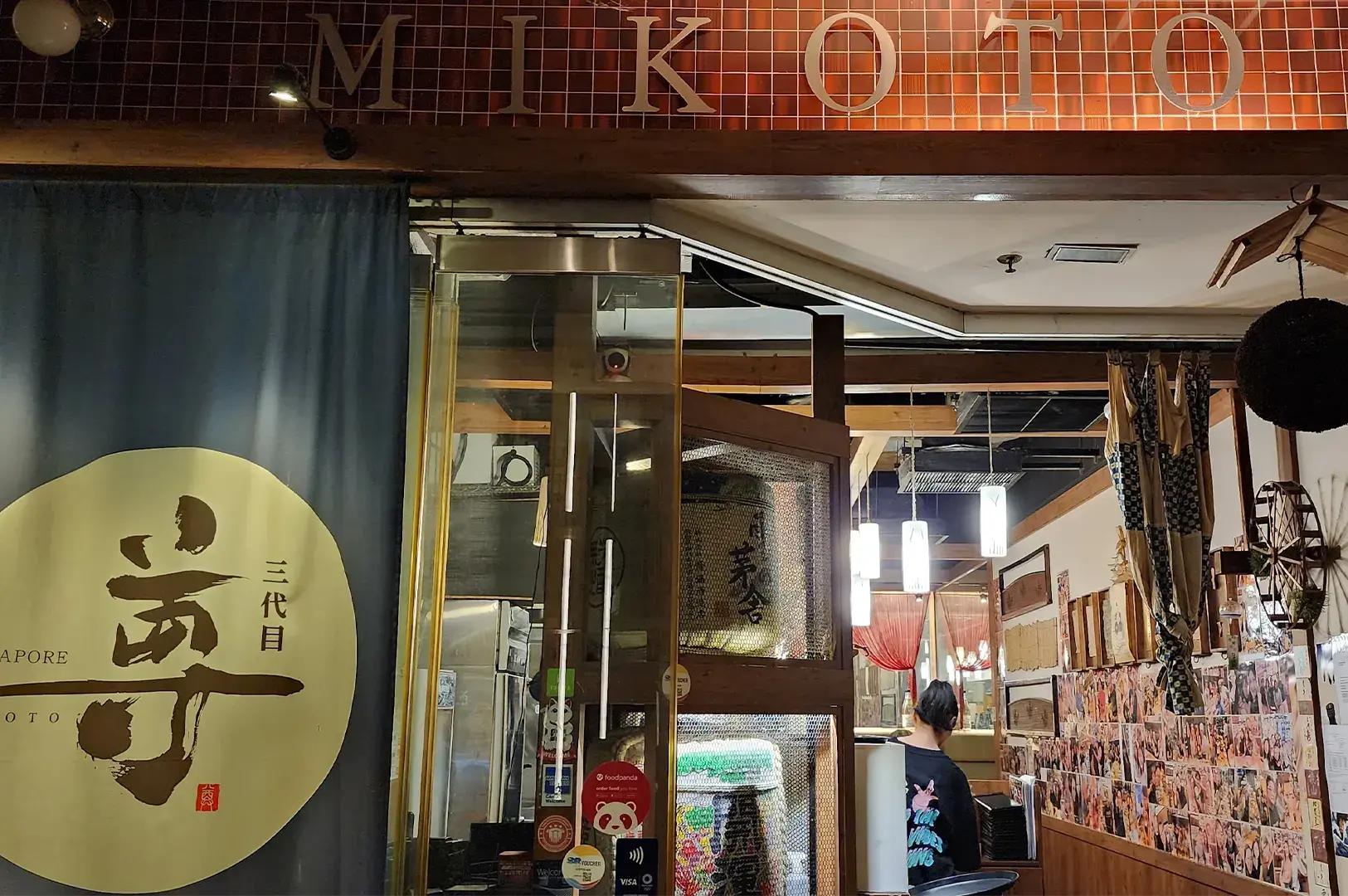 Exterior view of Mikoto Japanese restaurant storefront with traditional noren banners and sake barrels displays.