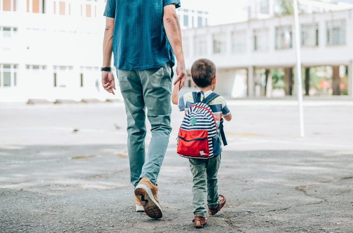 Dad holding his little boy's hand and walking him to school. 