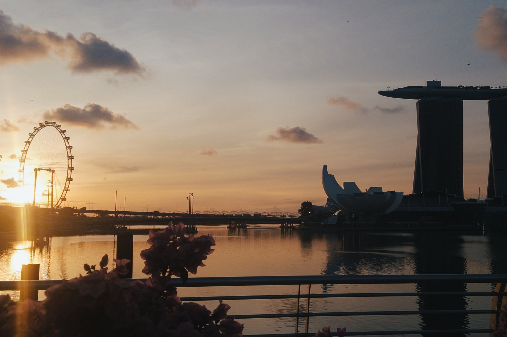 Sunrise view of Marina Bay Sands and the Singapore Flyer reflecting on calm waterfront waters.