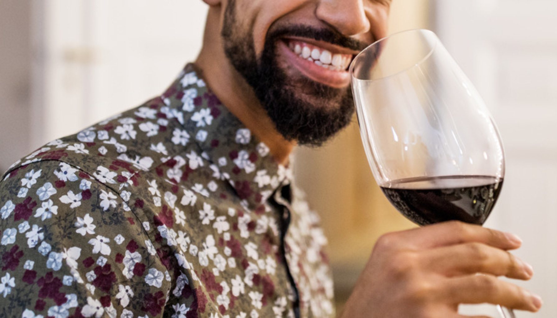 Smilende mann i blomstrete skjorte holder vinglass med rødvin i hånden.