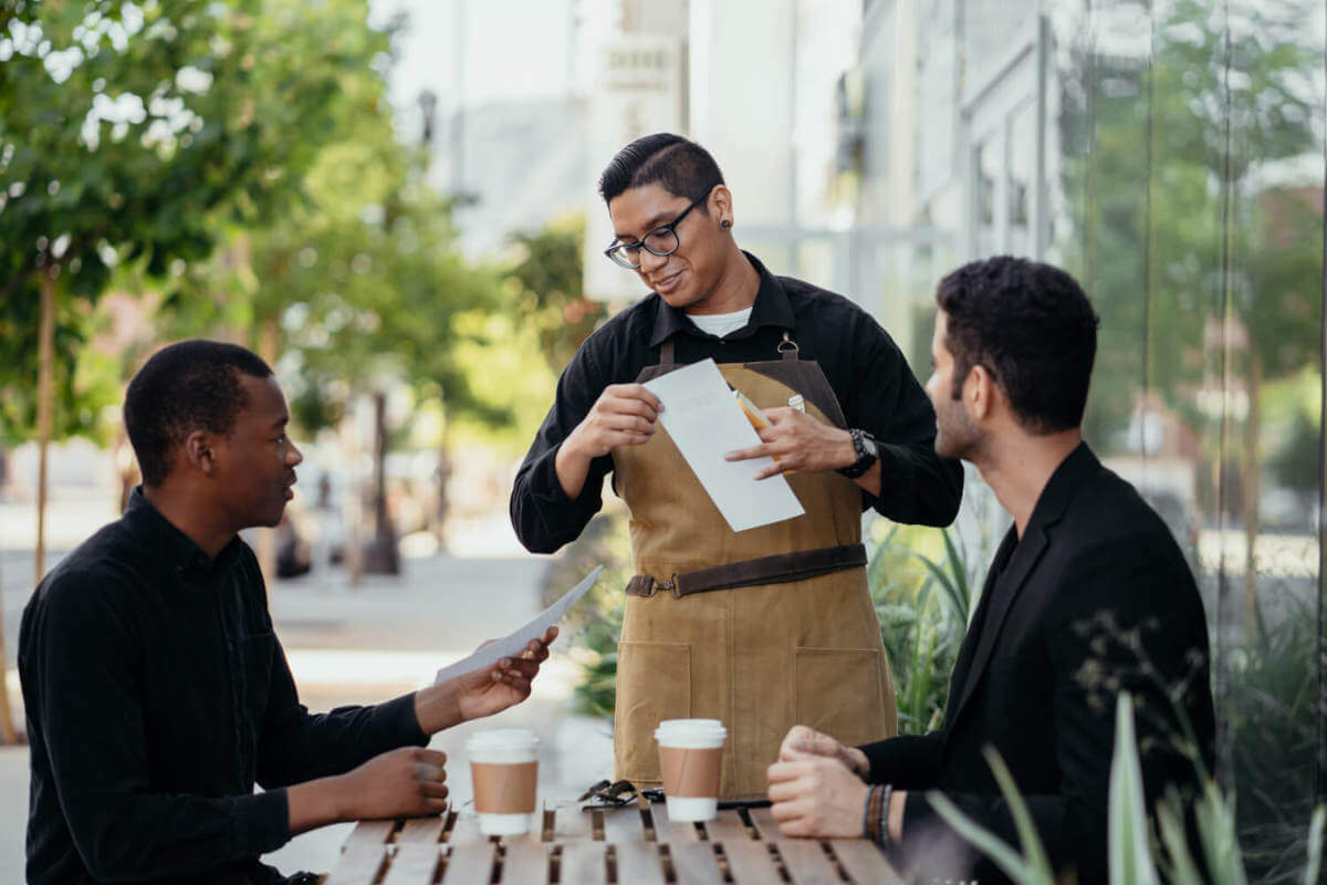 a waiter serving two men outside at a coffee shop