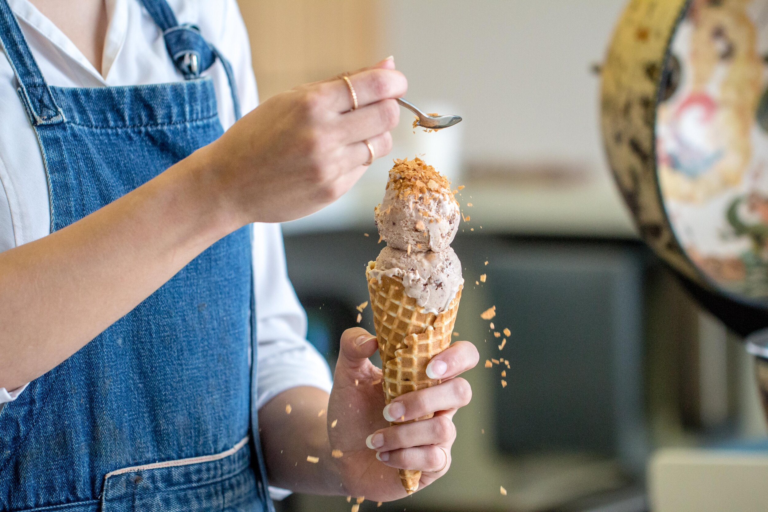 Person pouring corn flake crumbs on ice cream cone
