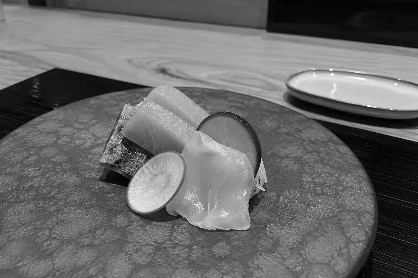 Small assortment of sashimi arranged on a textured ceramic plate with citrus slices and a decorative garnish.
