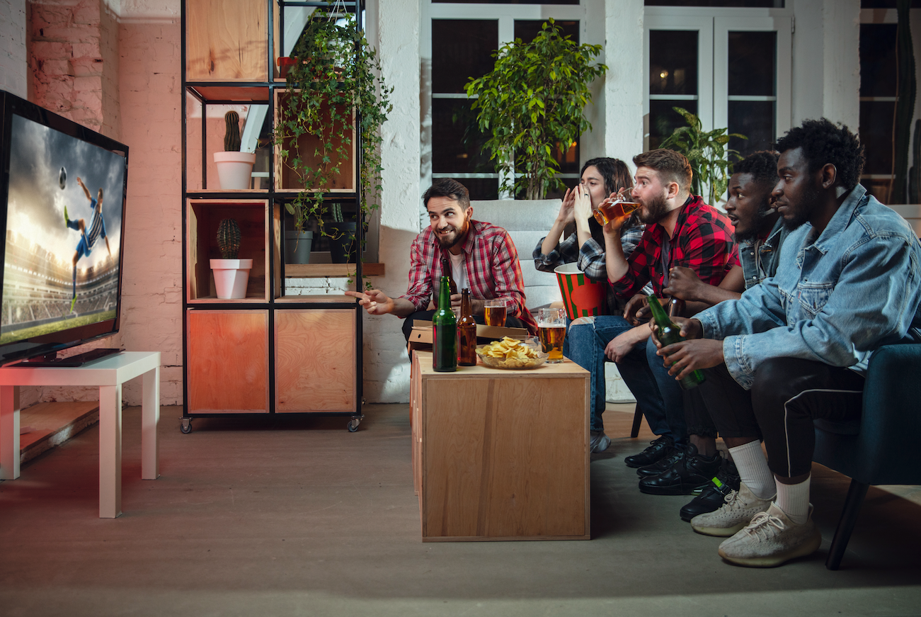 five people are watching a soccer game on the tv while sitting on a couch in an apartment