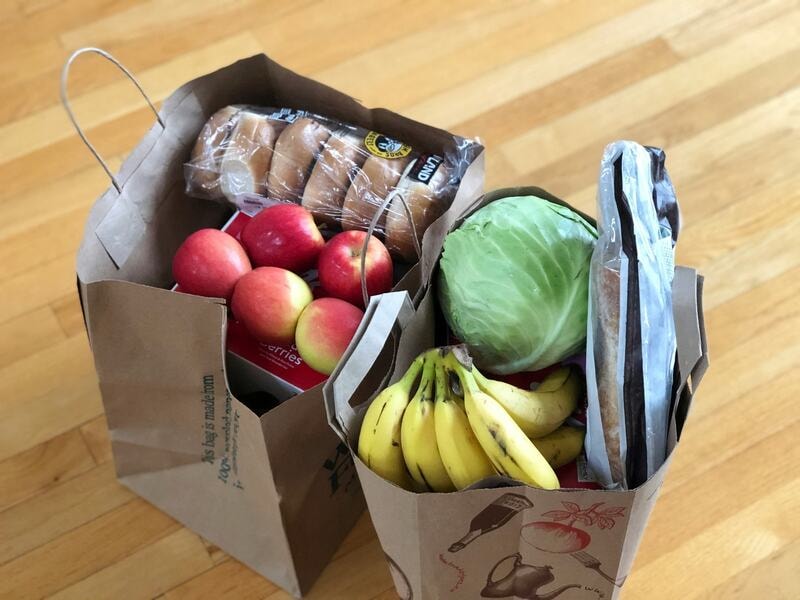 Grocery bags made of paper. They contain fresh produce and essentials, including apples, bananas, cabbage, bread, and bagels. These strong, sustainable bags provide reliable support for heavy loads, promoting sustainable shopping practices while keeping food organized and easy to carry home.