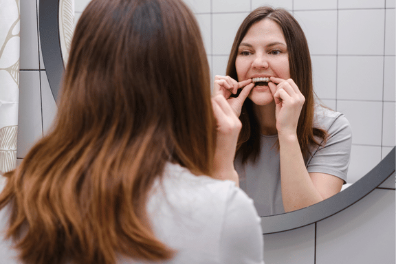 a women inserting a clear aligner on her upper teeth looking in a mirror