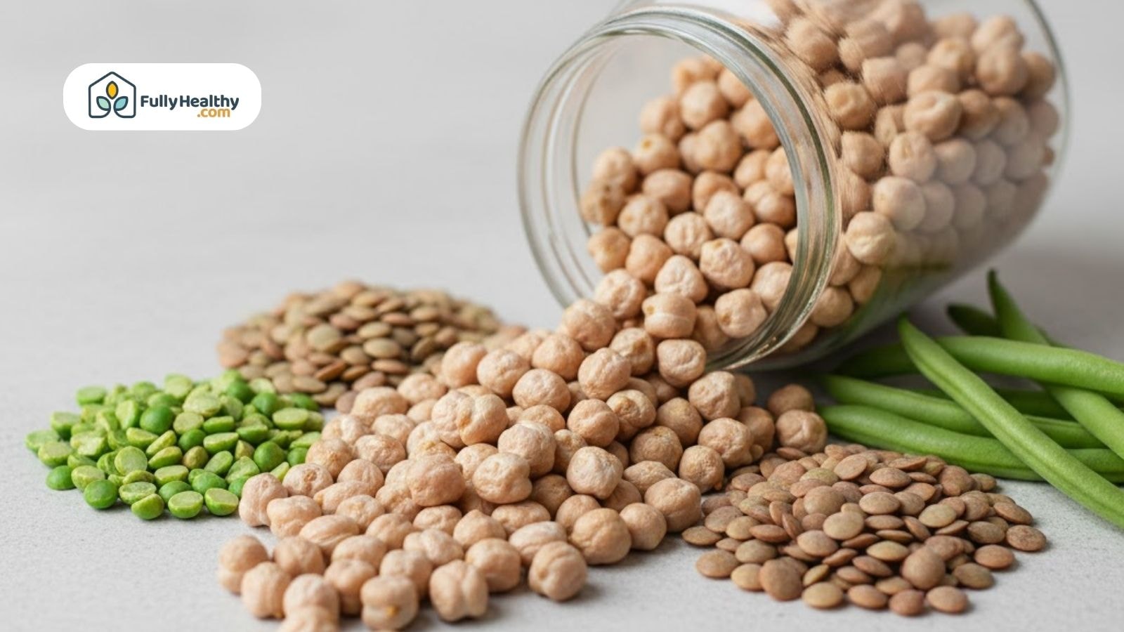 Dried chickpeas spilling from a glass jar alongside lentils and green peas.