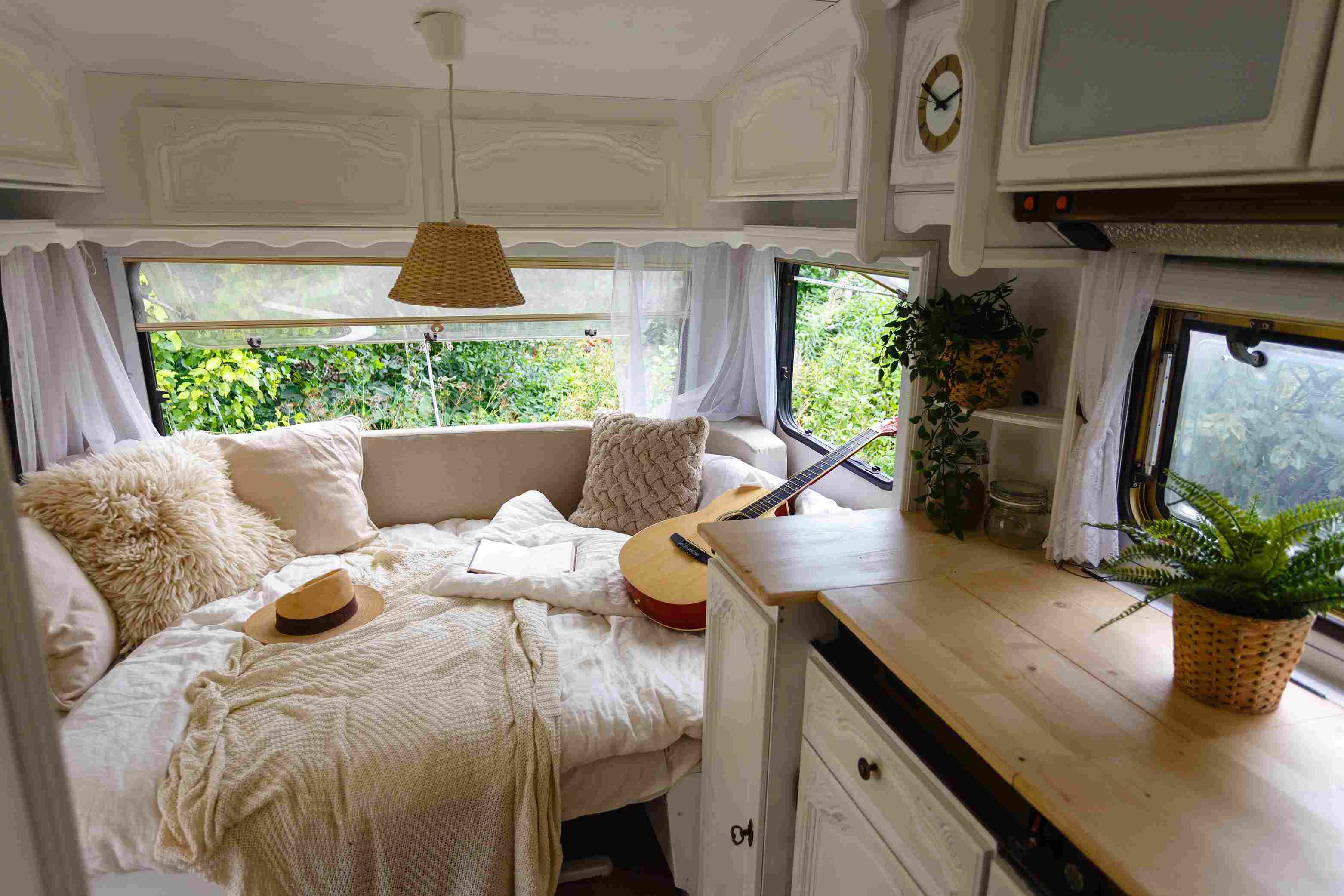 Wnętrze przyczepy kempingowej: biała drewniana boazeria, jasne poduszki i wełniane koce