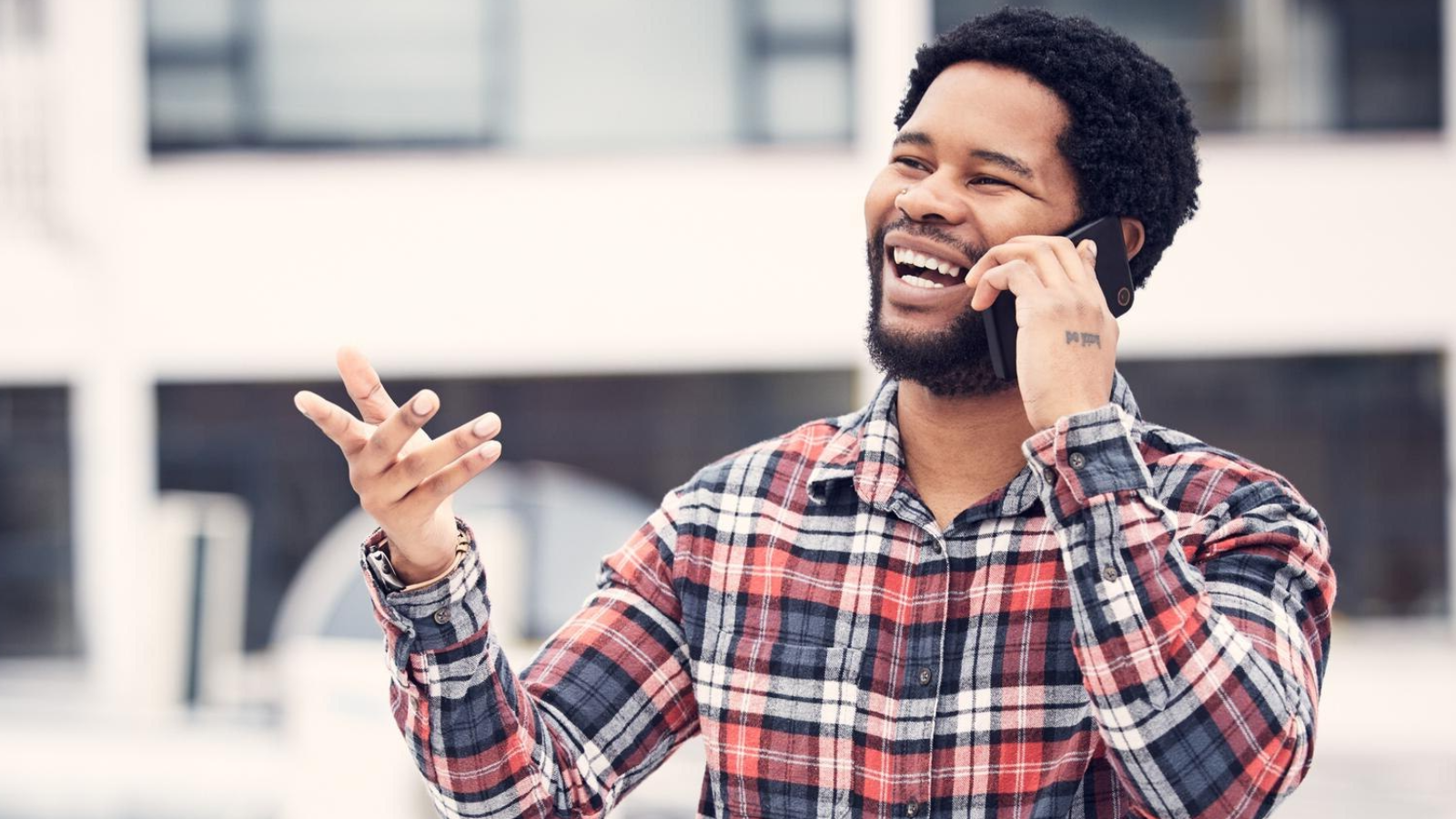 Man in a plaid shirt laughing on a cell phone, demonstrating the real-world benefits and flexibility of business VoIP for client calls and new locations.