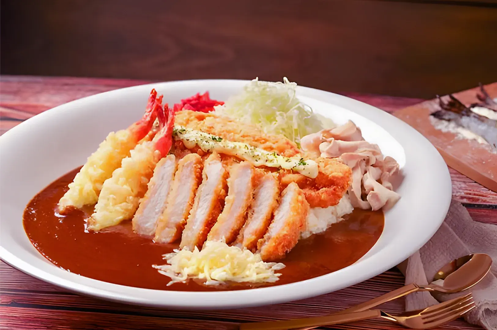 Overhead shot of Japanese curry katsu rice with crispy cutlet, accompanied by pasta, salad, and traditional side dishes on a wooden table.