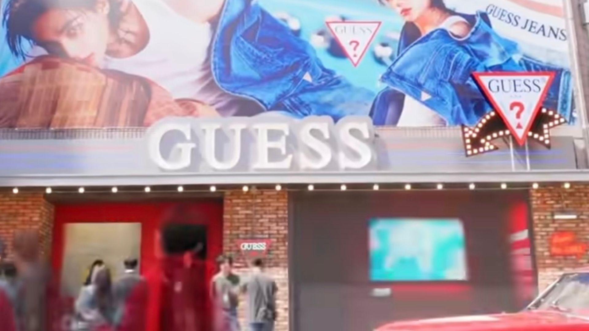 A big billboard sign is on top of a red brick building that has GUESS marketing.