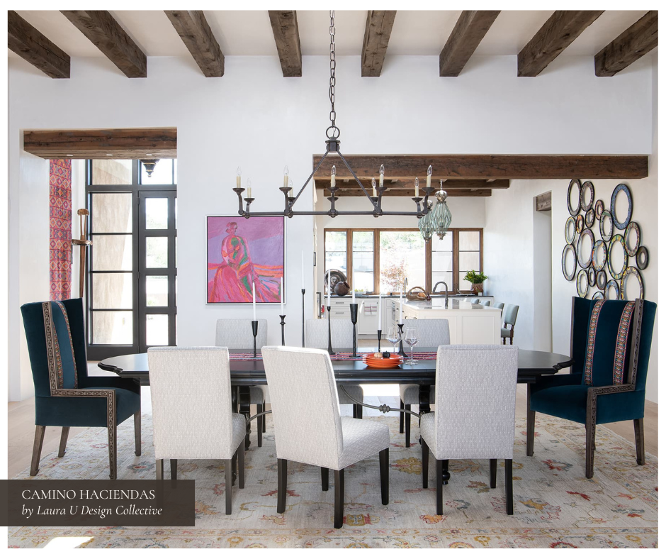 Warm and colorful Southwestern-style dining room with rustic wood ceiling beams, a mix of upholstered and wingback chairs, iron chandelier, tribal rug, and vibrant artwork that ties the space to its Santa Fe surroundings.