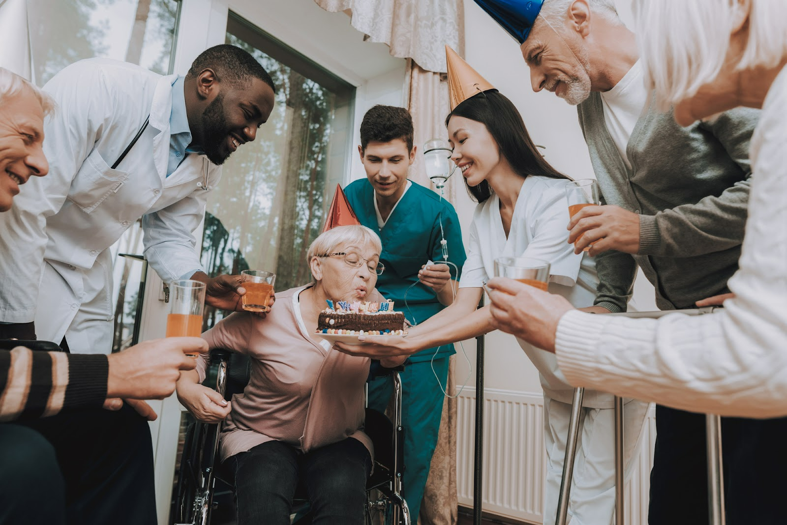 Guests celebrating in a circle and holding a birthday cake for an older adult to blow the candles out