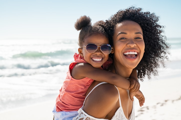 Beautiful young mom carrying her daughter on the beach. 