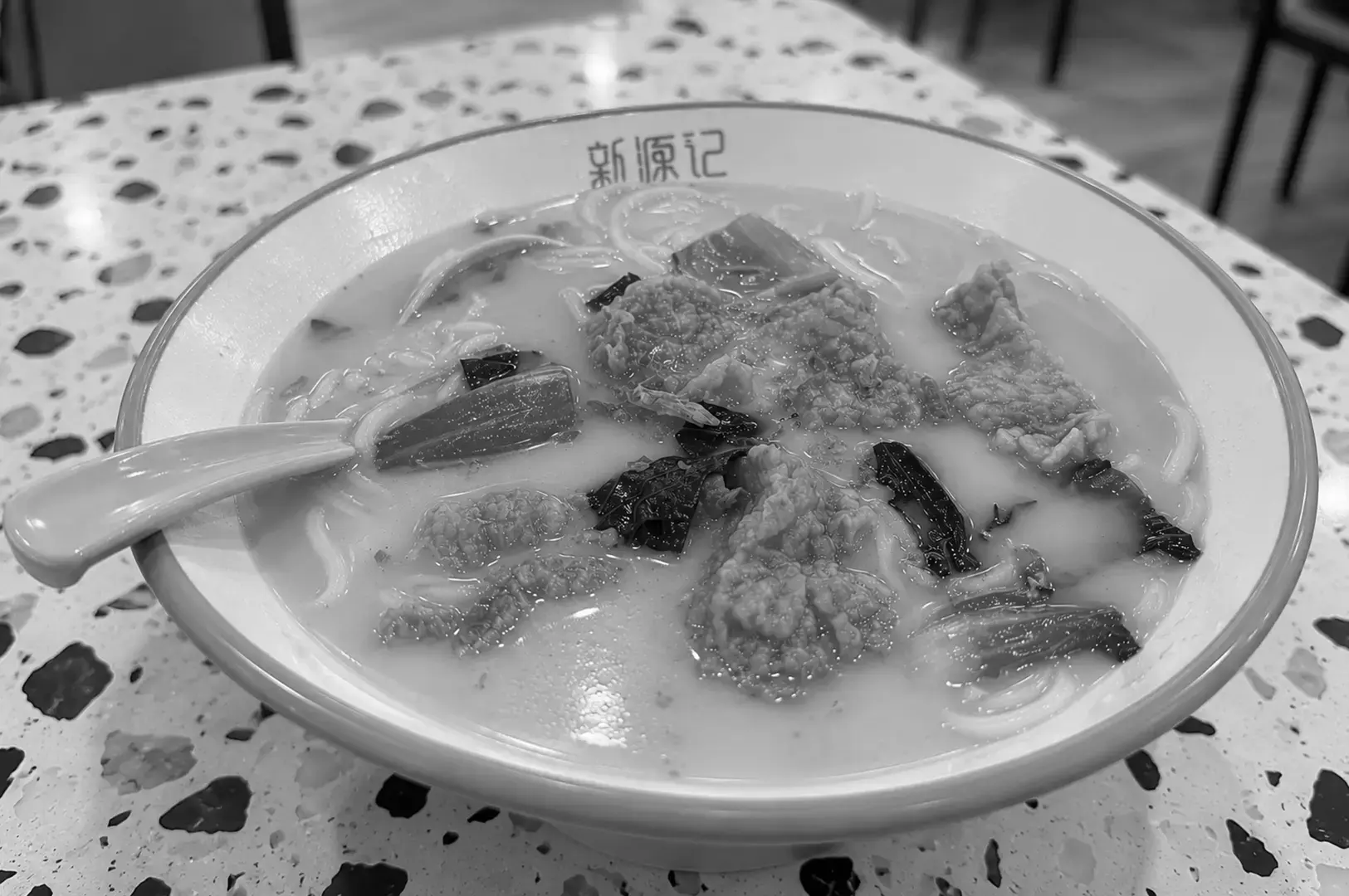 A bowl of Sliced Fish Soup with thin fish slices, leafy greens, and noodles served in a light, milky broth.