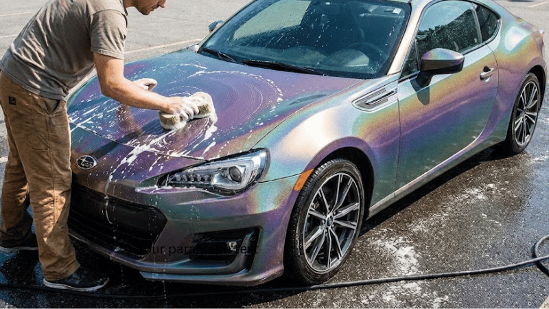 A man is washing the car with iridescent wrap.