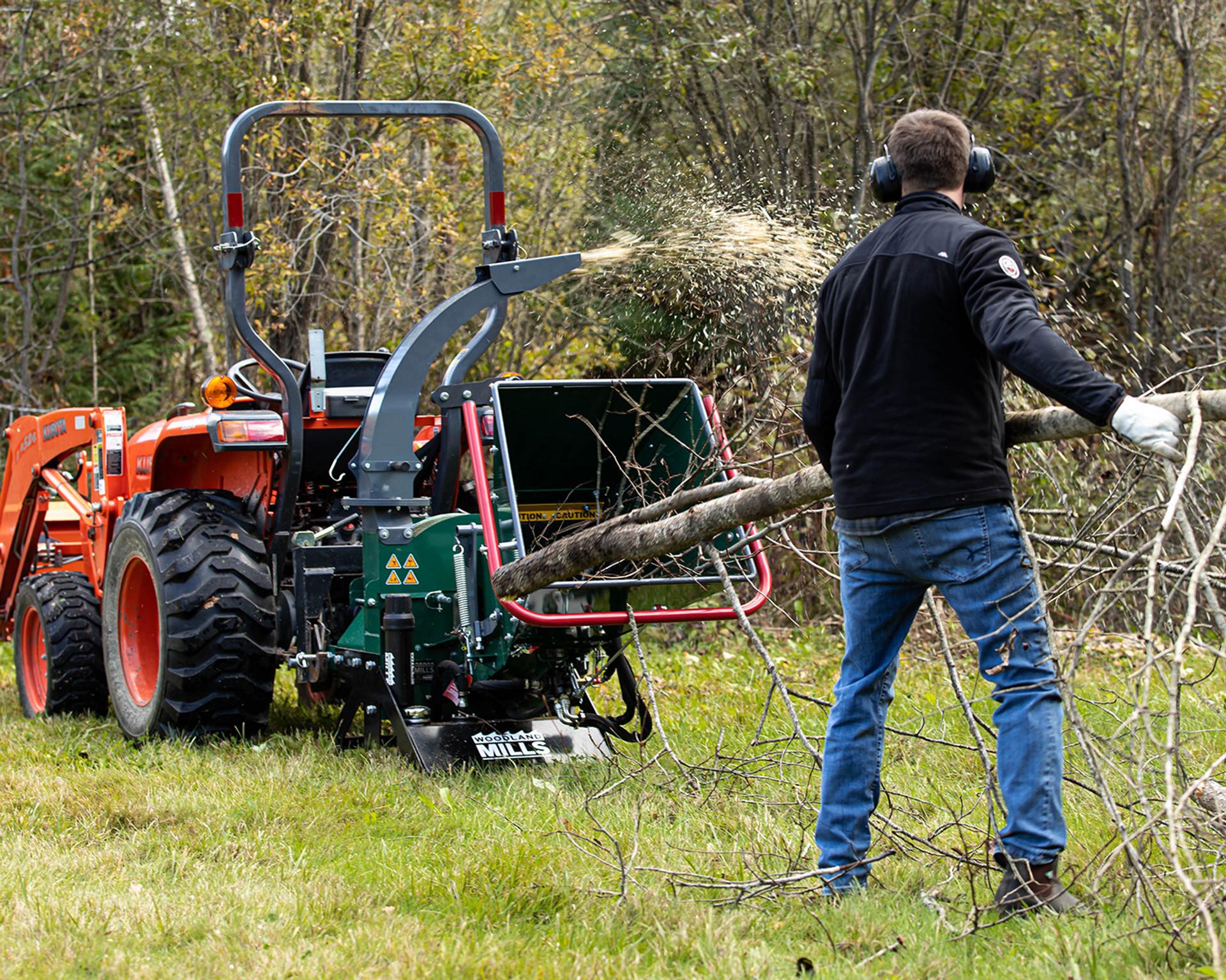 A landowner feeding a large tree branch into a Woodland Mills wood chipper.