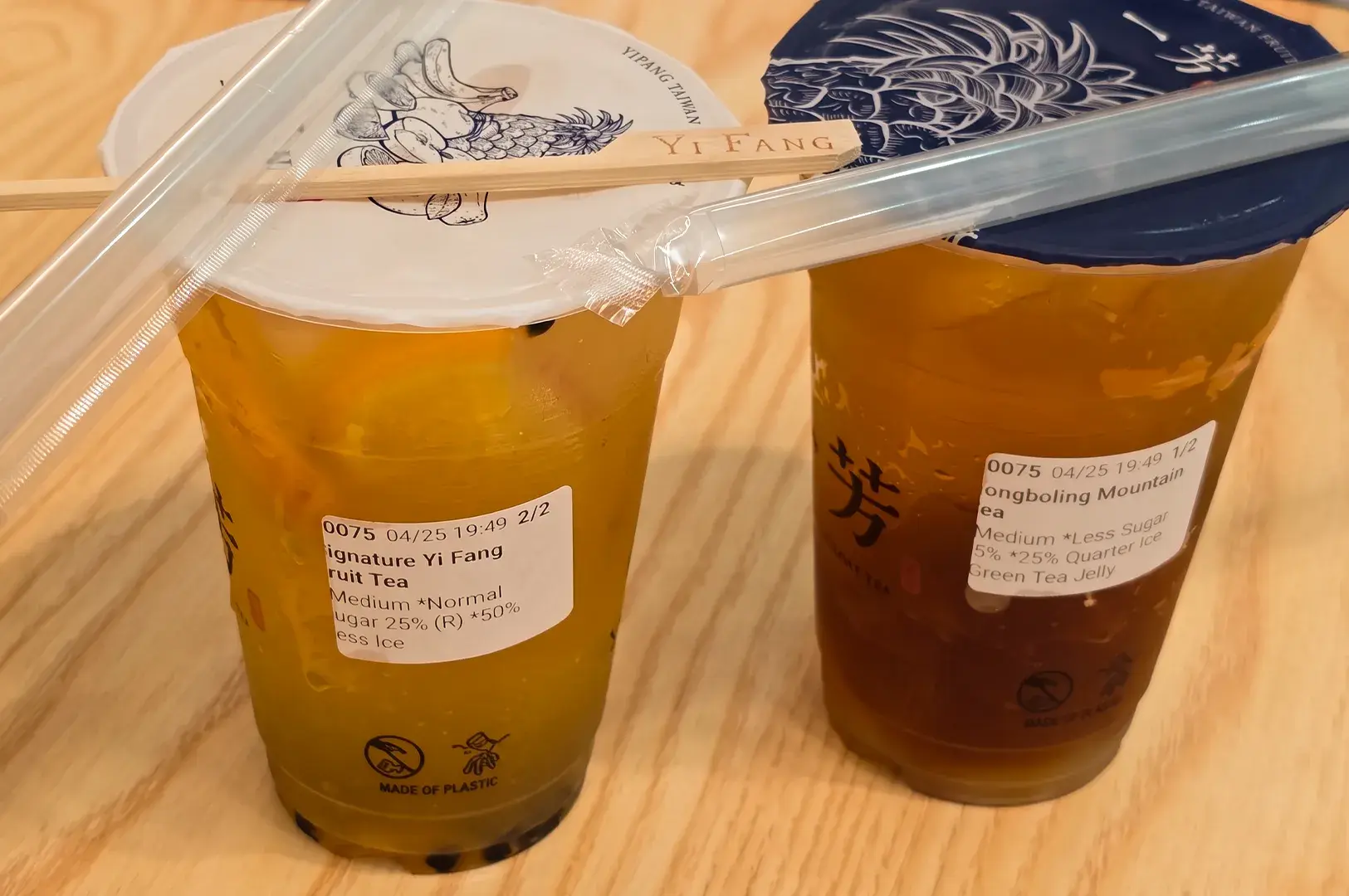 Two sealed Yi Fang Taiwan Fruit Tea cups with custom order labels and wrapped straws sitting on a wooden table.