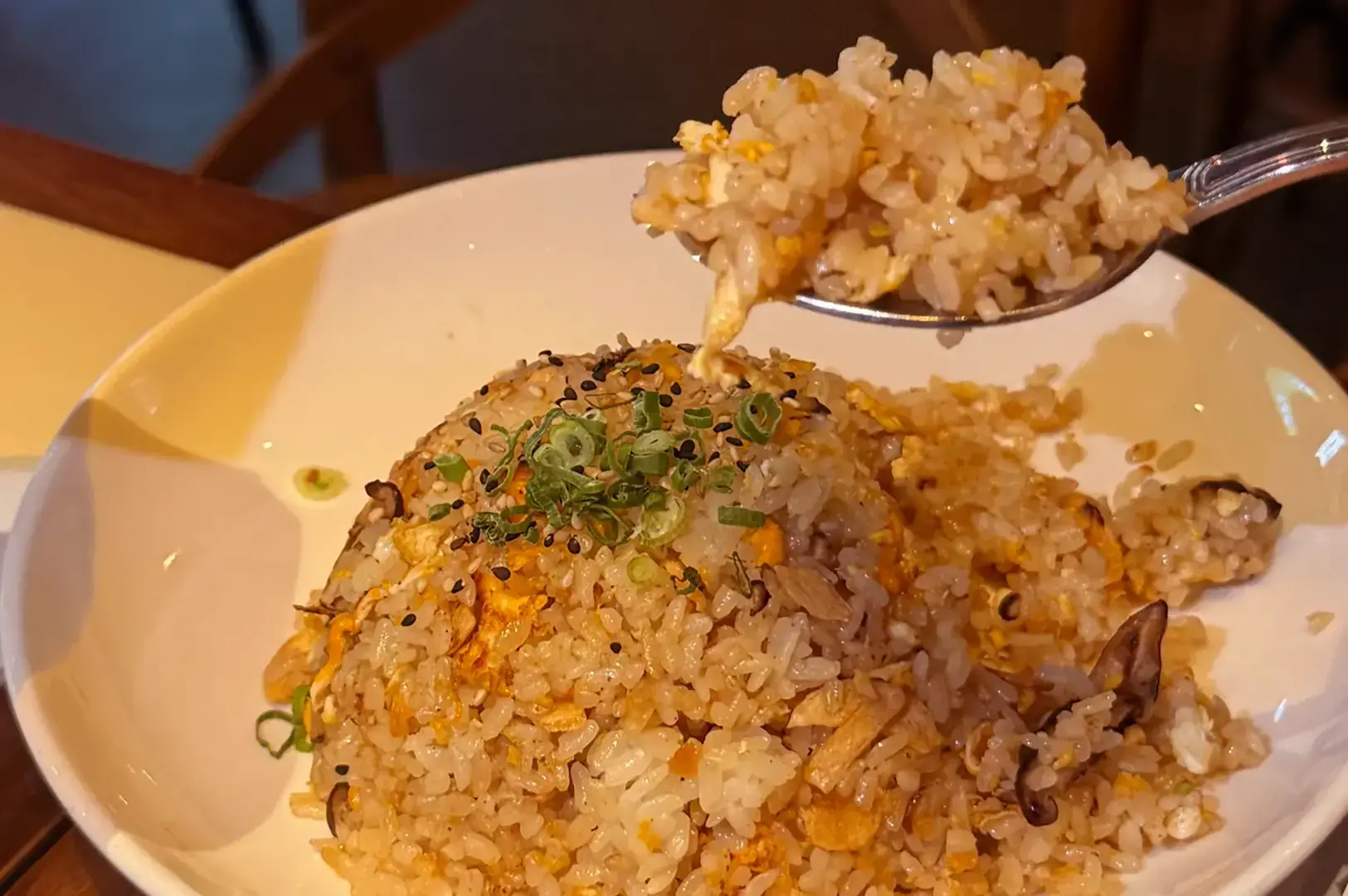 Fried rice topped with chopped green onions and sesame seeds, with a spoonful lifted above the plate.