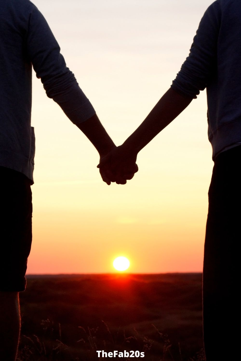Couple holding hands looking at sunset