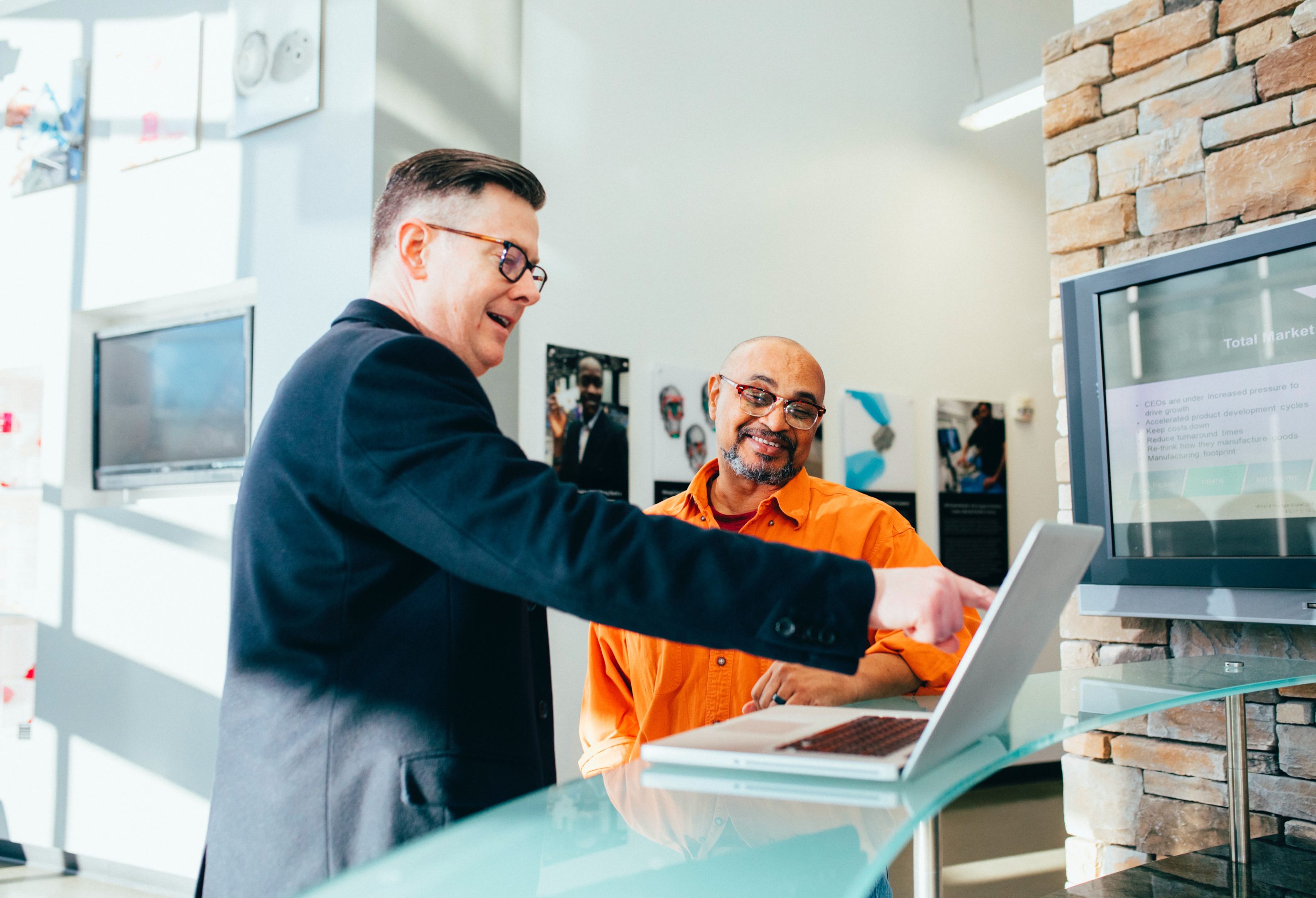 Photo of two people in corporate attire while smiling and pointing to a laptop.