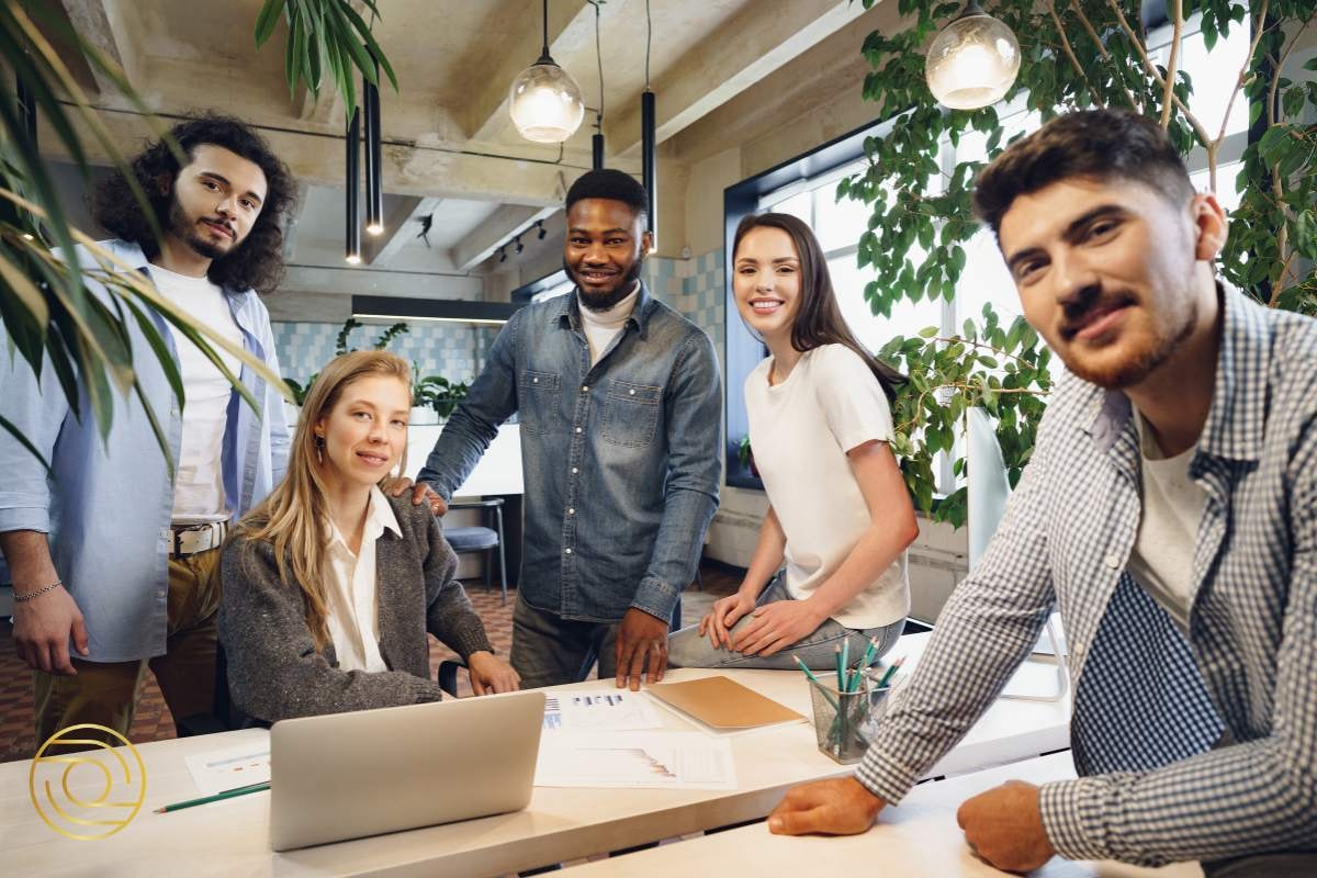 Five team members gathered around a desk, smiling and collaborating on a project, emphasising the power of teamwork and shared strengths.