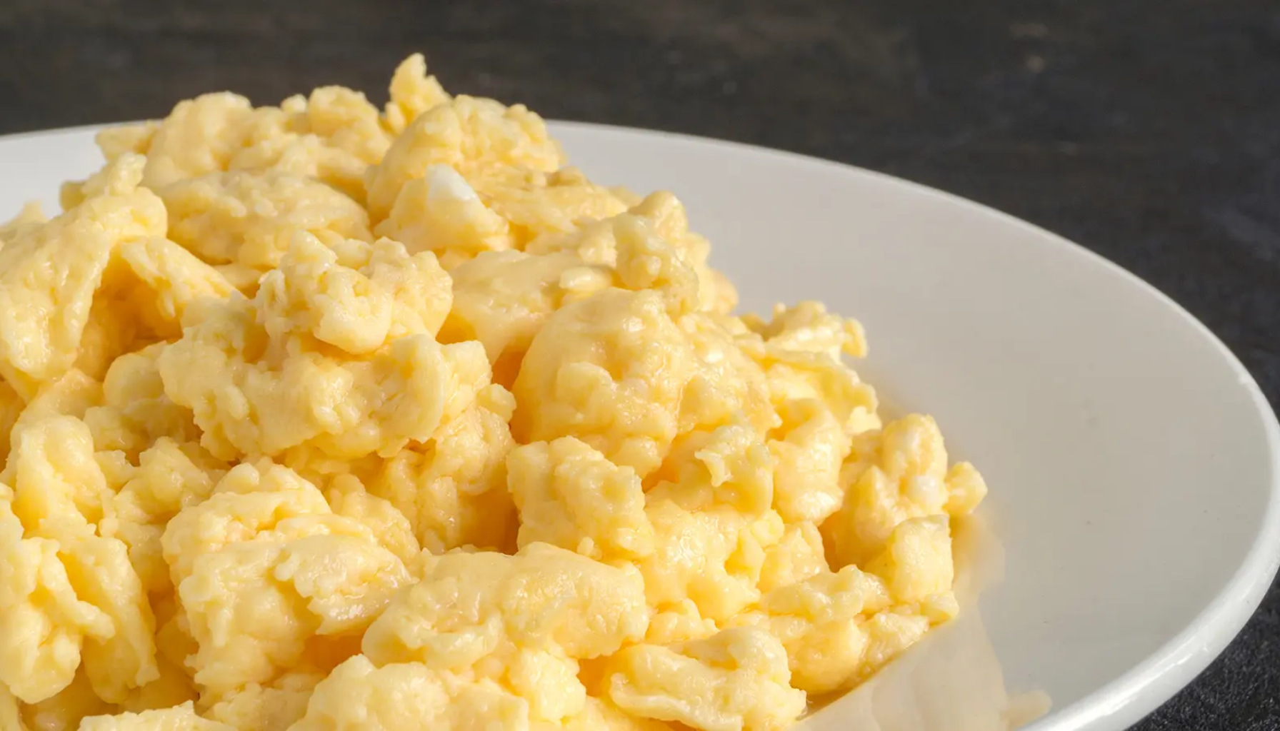 Nærbilde av eggerøre servert på en hvit tallerken, med mørk bakgrunn som fremhever den kremete konsistensen og den gylne fargen.