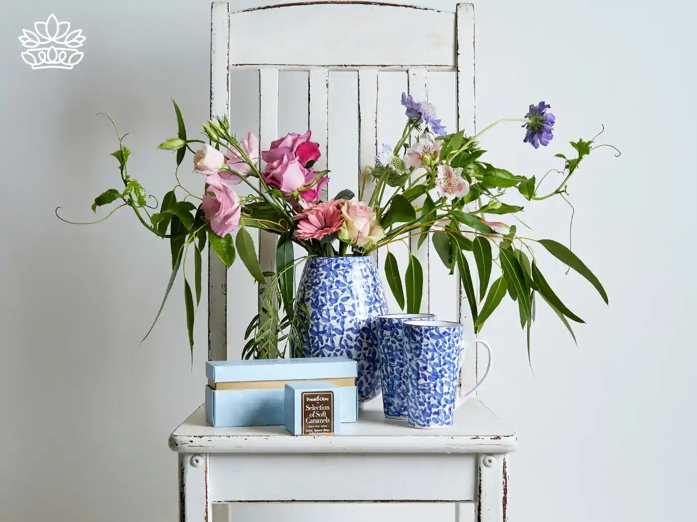Floral arrangement with matching blue and white mugs, and a selection of soft caramels on a vintage white chair. Gift Boxes for Sister. Delivered with Heart. Fabulous Flowers and Gifts.
