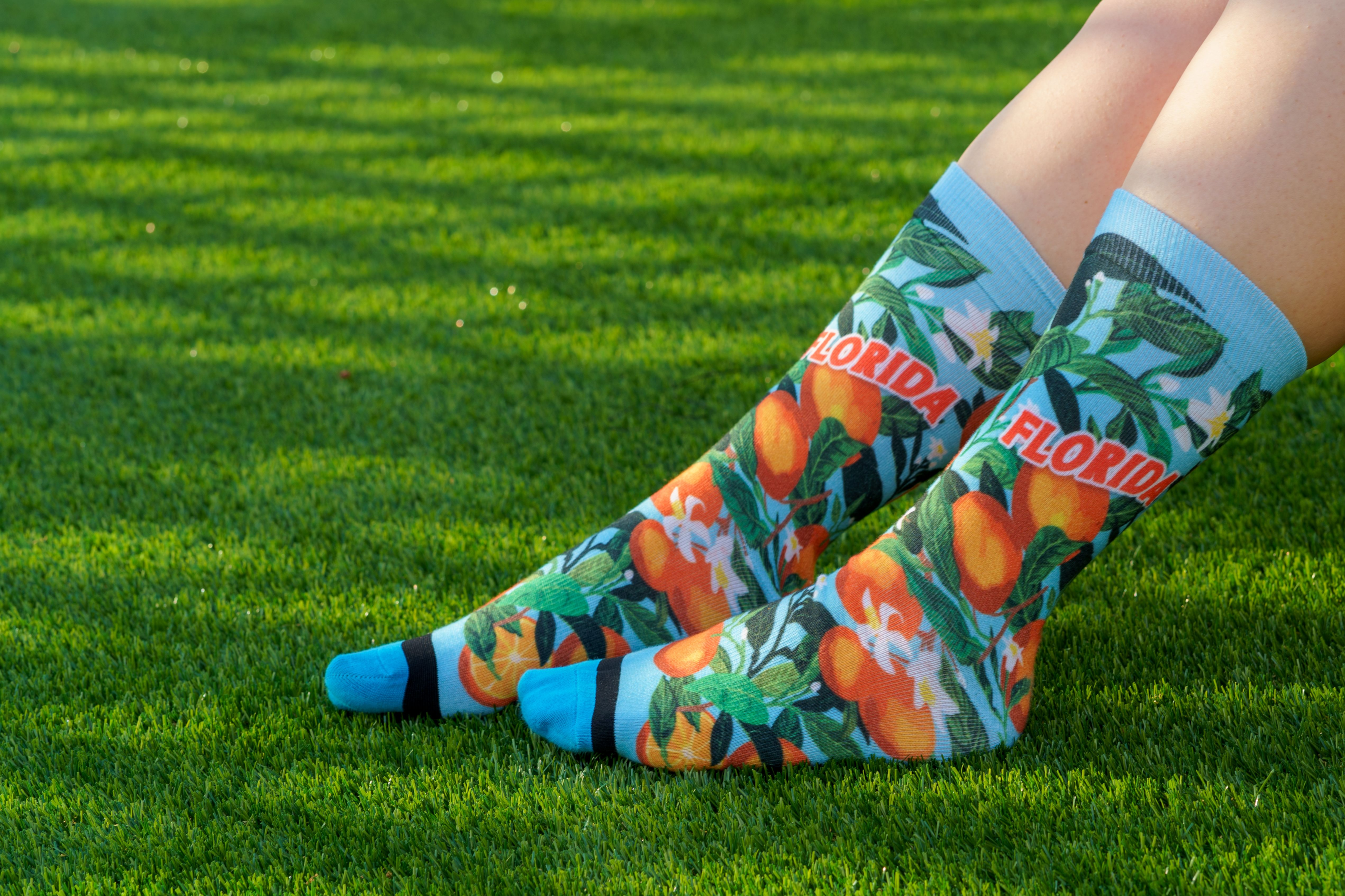 Blue socks with the word "Florida" on top of bright, beautiful oranges and orange blossoms. 