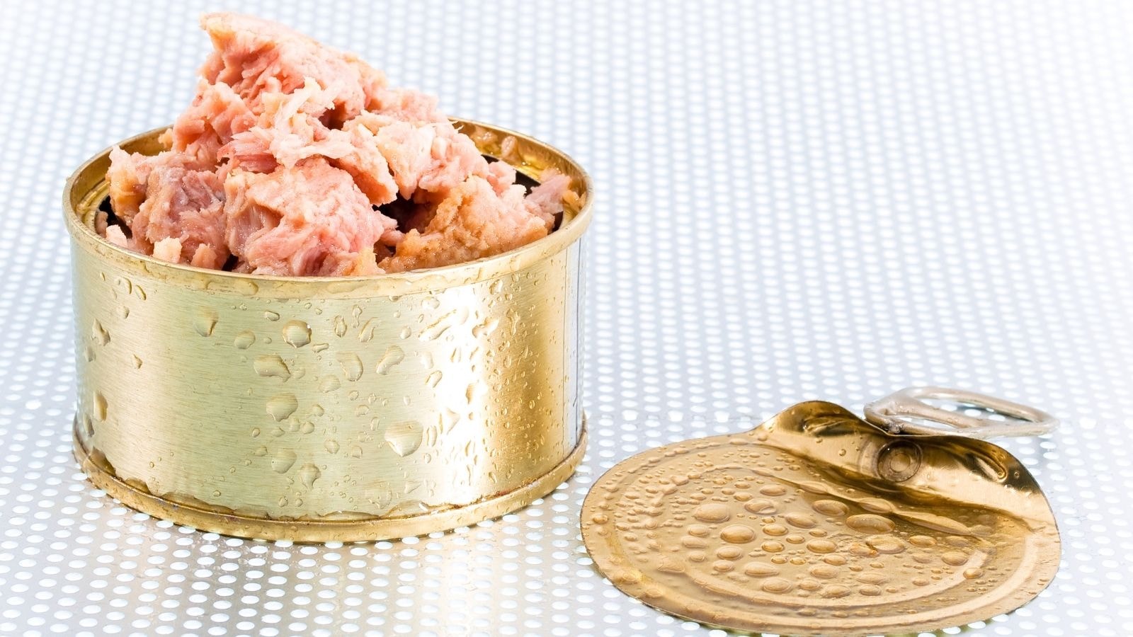 Open canned tuna showing pink chunks of fish with moisture on metal surface