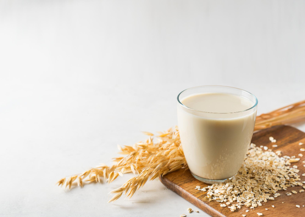 A glass of oat milk on a wooden board with some oats scattered around it.