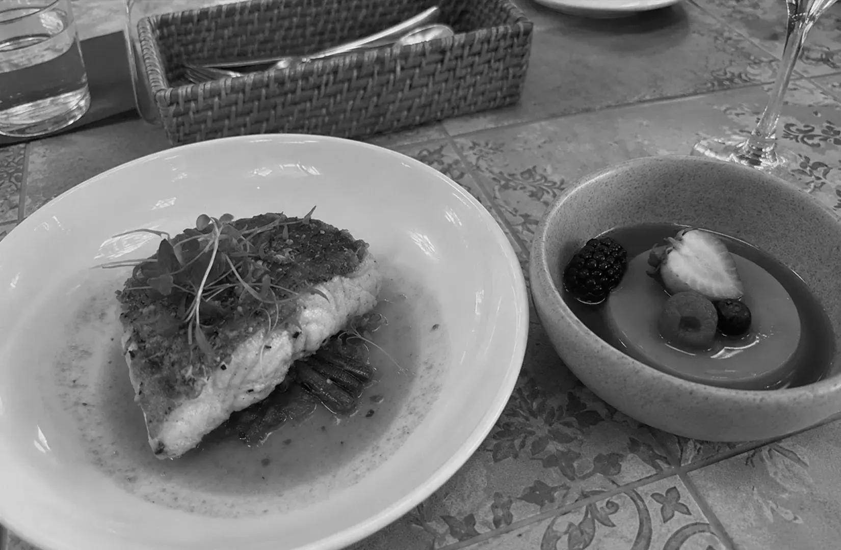 Grilled fish served with vegetables alongside a fruit dessert at a restaurant table.
