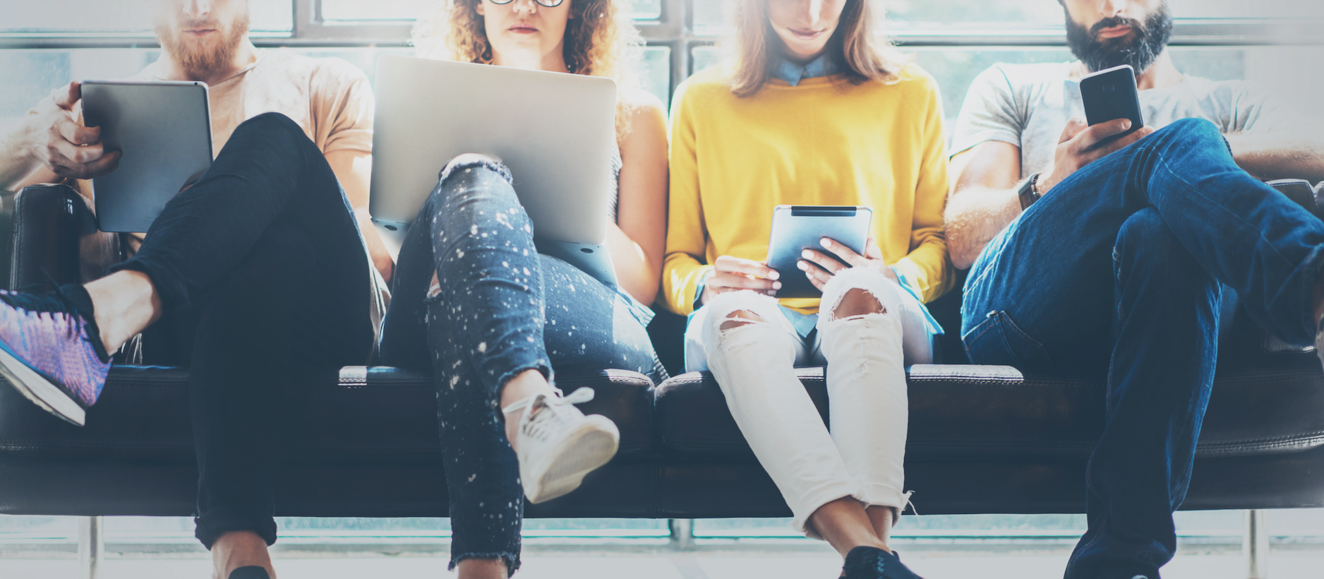 four people casually browse internet connected devices while sitting next to each other in public