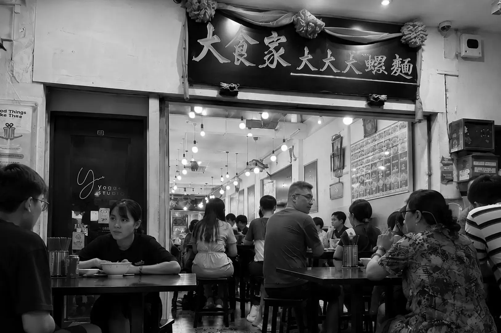 Busy prawn noodle restaurant with diners seated under a traditional Chinese signboard.