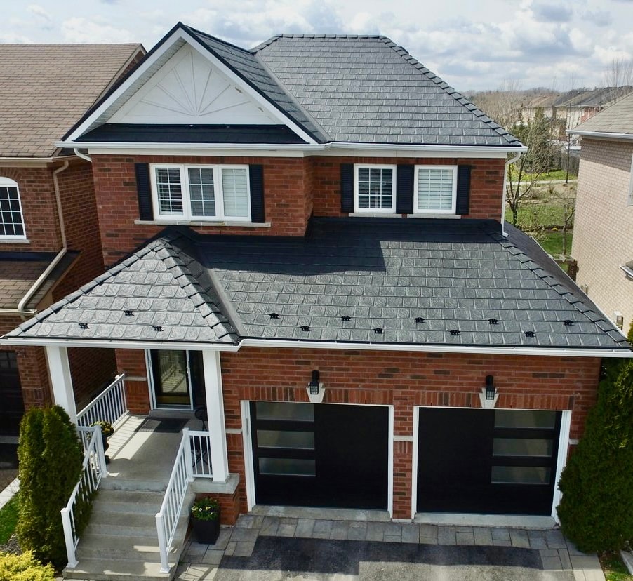 A picture of a home with a dark roof, which reinforces the idea that dark roofs are better for heat absorption within the home. The home is situated in a neighbourhood and is surrounded by other homes.