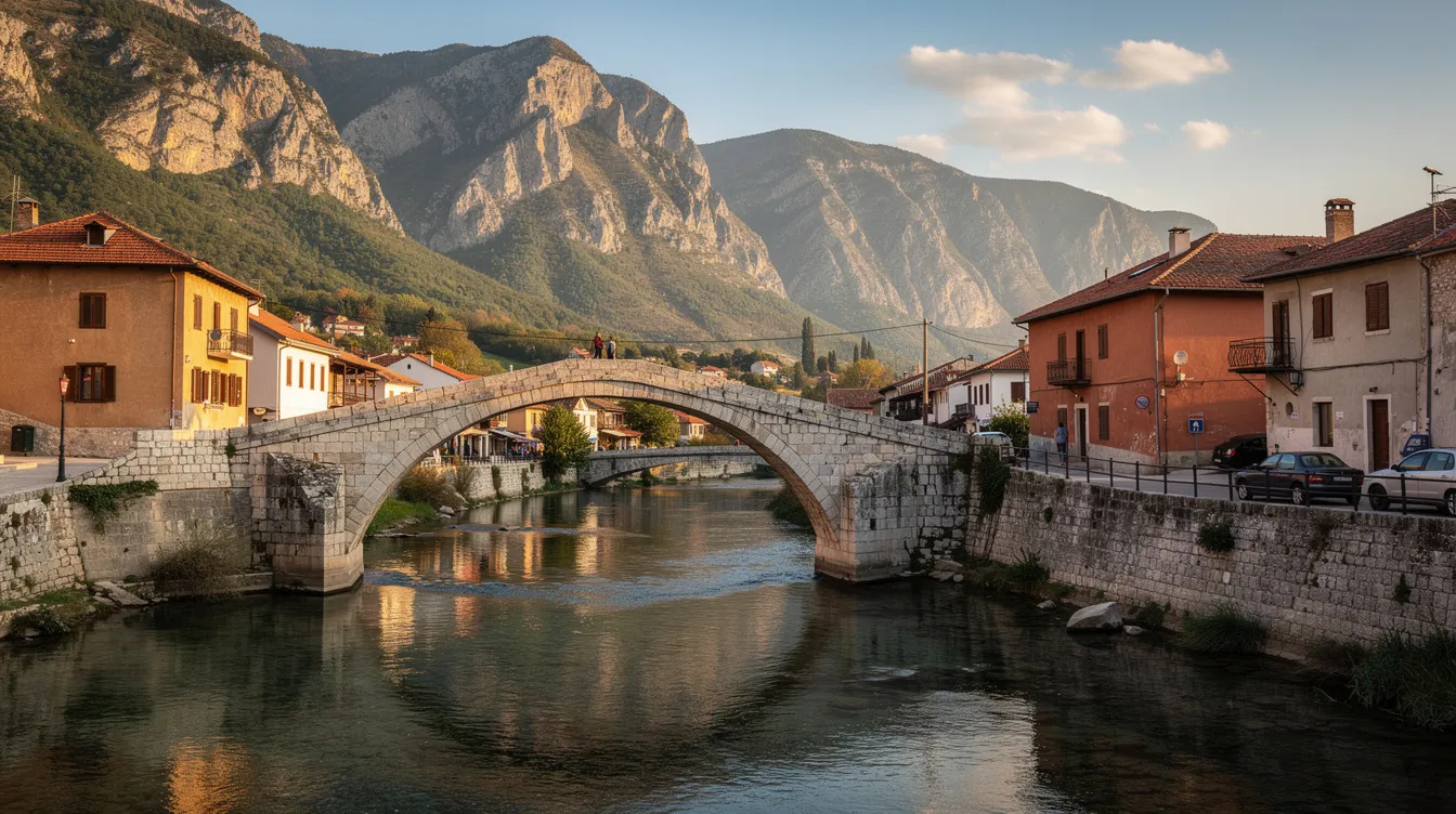A imagem mostra uma antiga ponte de pedra sobre um rio em uma cidade balcânica, com montanhas ao fundo, evocando a beleza natural da Croácia. O cenário reflete a rica cultura e história da região, tornando-se um destino atraente para viagens e exploração.
