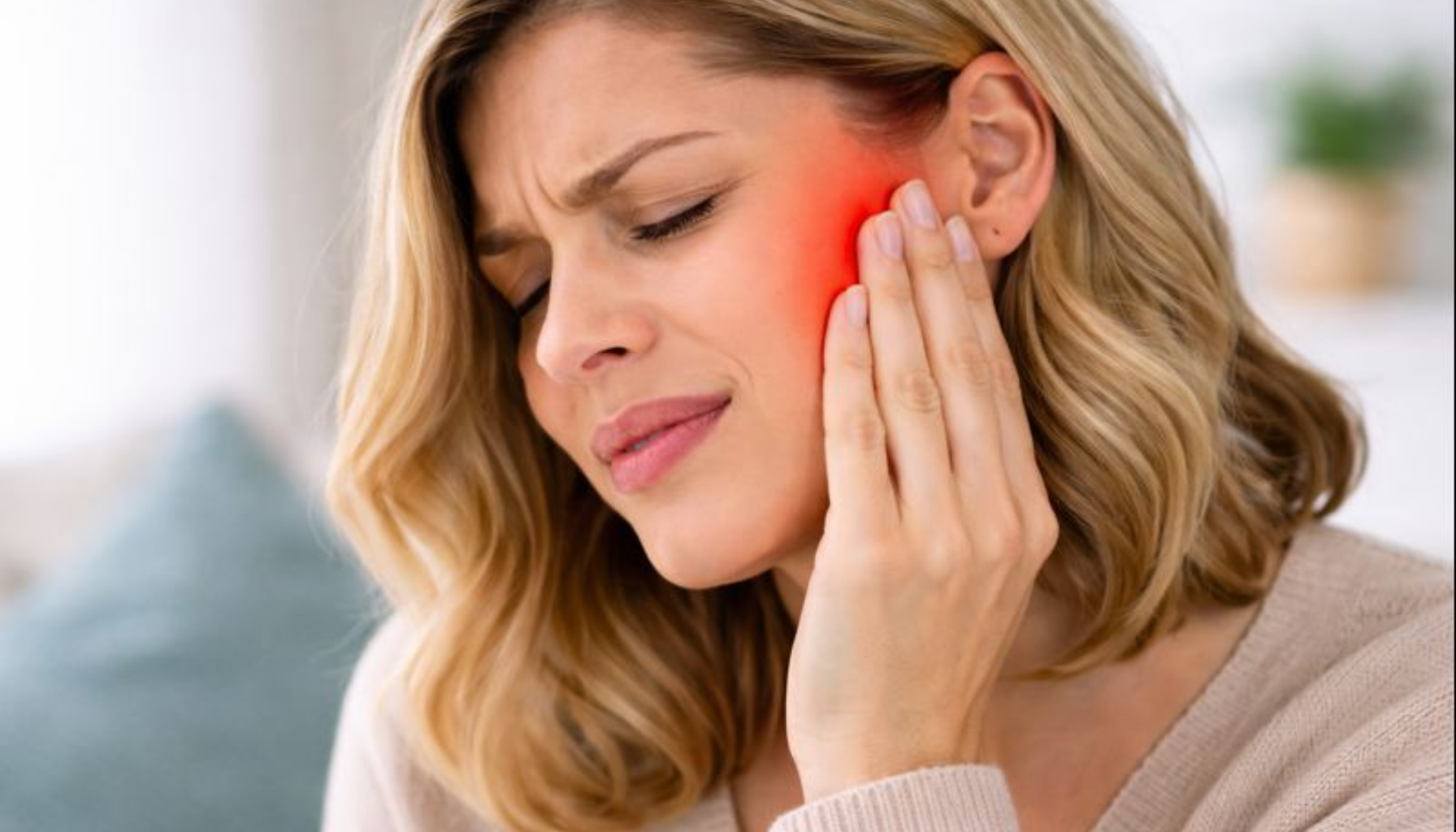 Kvinne holder kjeven med smerte, illustrerer temporomandibulær leddsmerte knyttet til hodepine og tannslitasje.