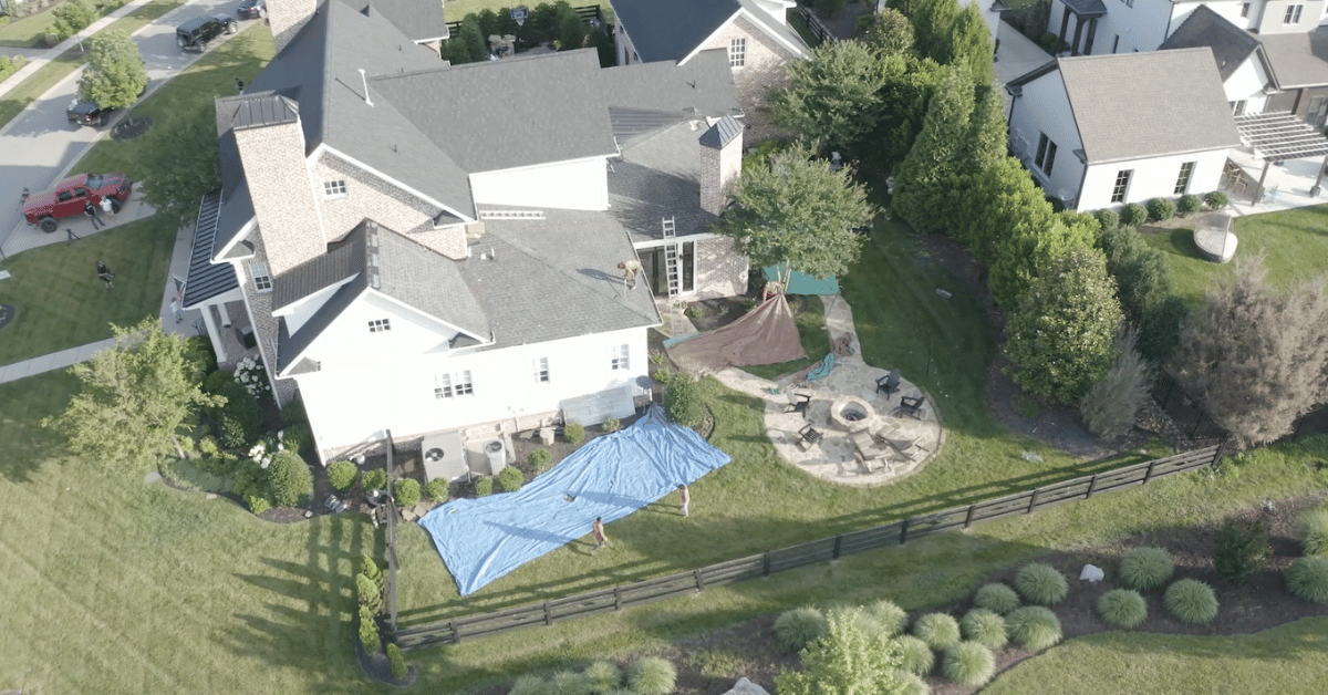 Overhead drone image showing complete site protection with tarps and debris barriers surrounding a large residential property during roof replacement.