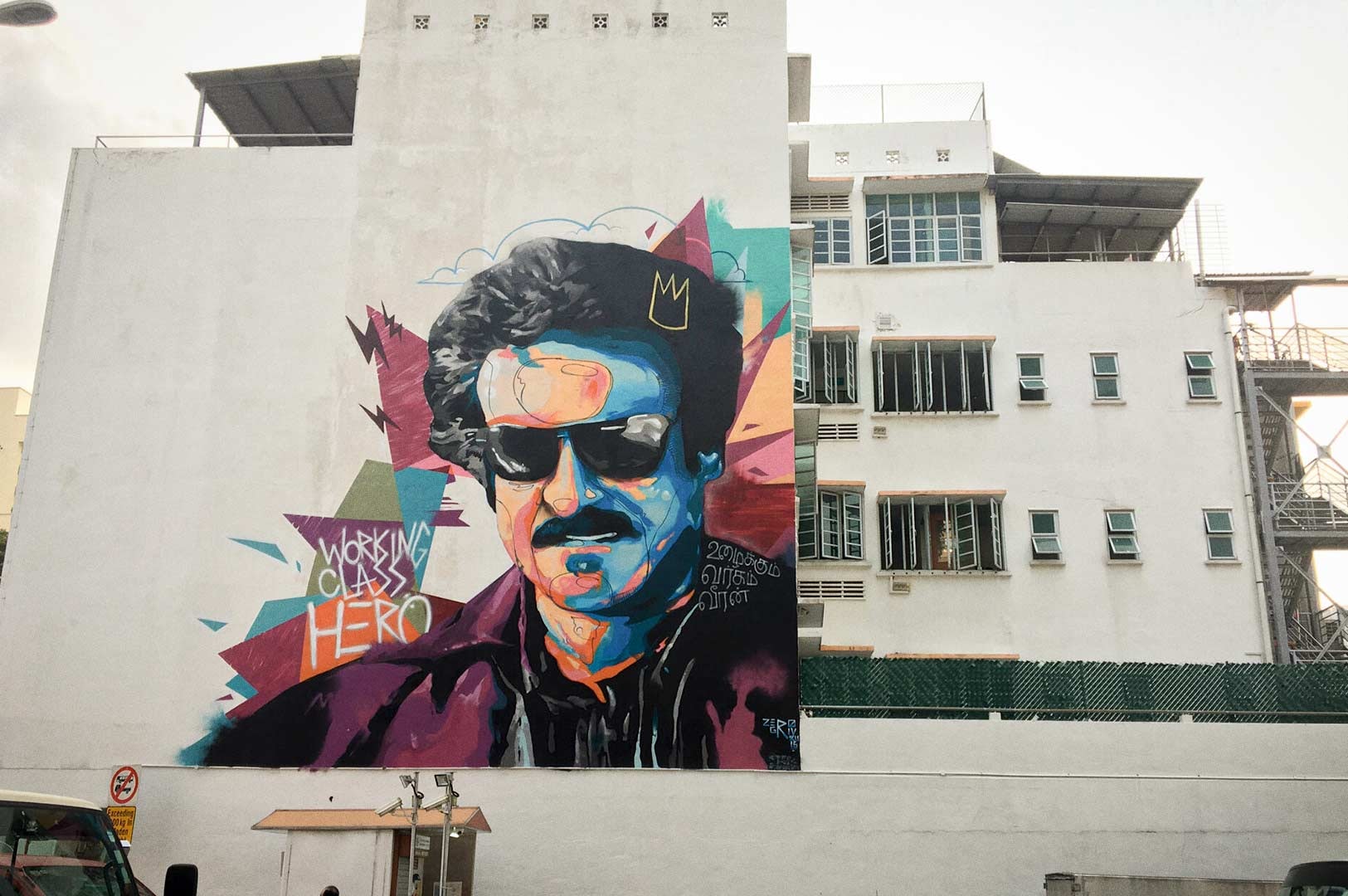 A large, colorful mural on the side of a building featuring bold abstract shapes, vibrant paint strokes, and the words “Working Class Hero” painted across the artwork.