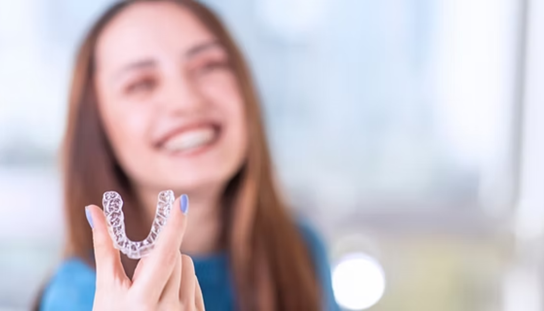 Smilende kvinne holder opp en gjennomsiktig tannskinne med hånden, klar til bruk for tannregulering.