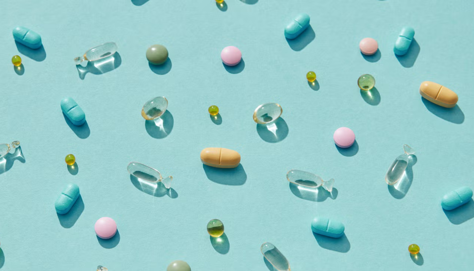 Ulike fargerike kosttilskudd og vitaminer spredt utover en lyseblå bakgrunn i naturlig dagslys.