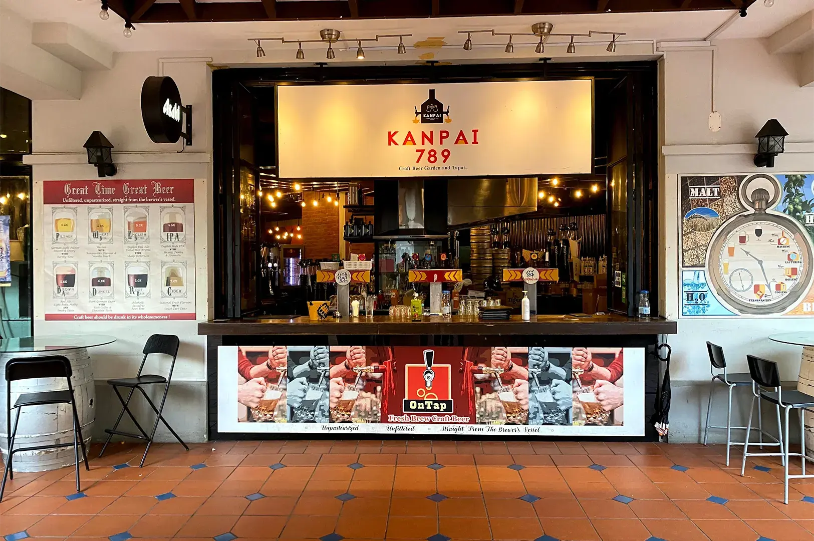 Outdoor bar counter of Kanpai 789 Craft Beer Garden and Tapas displaying beer tap handles and beverage posters.