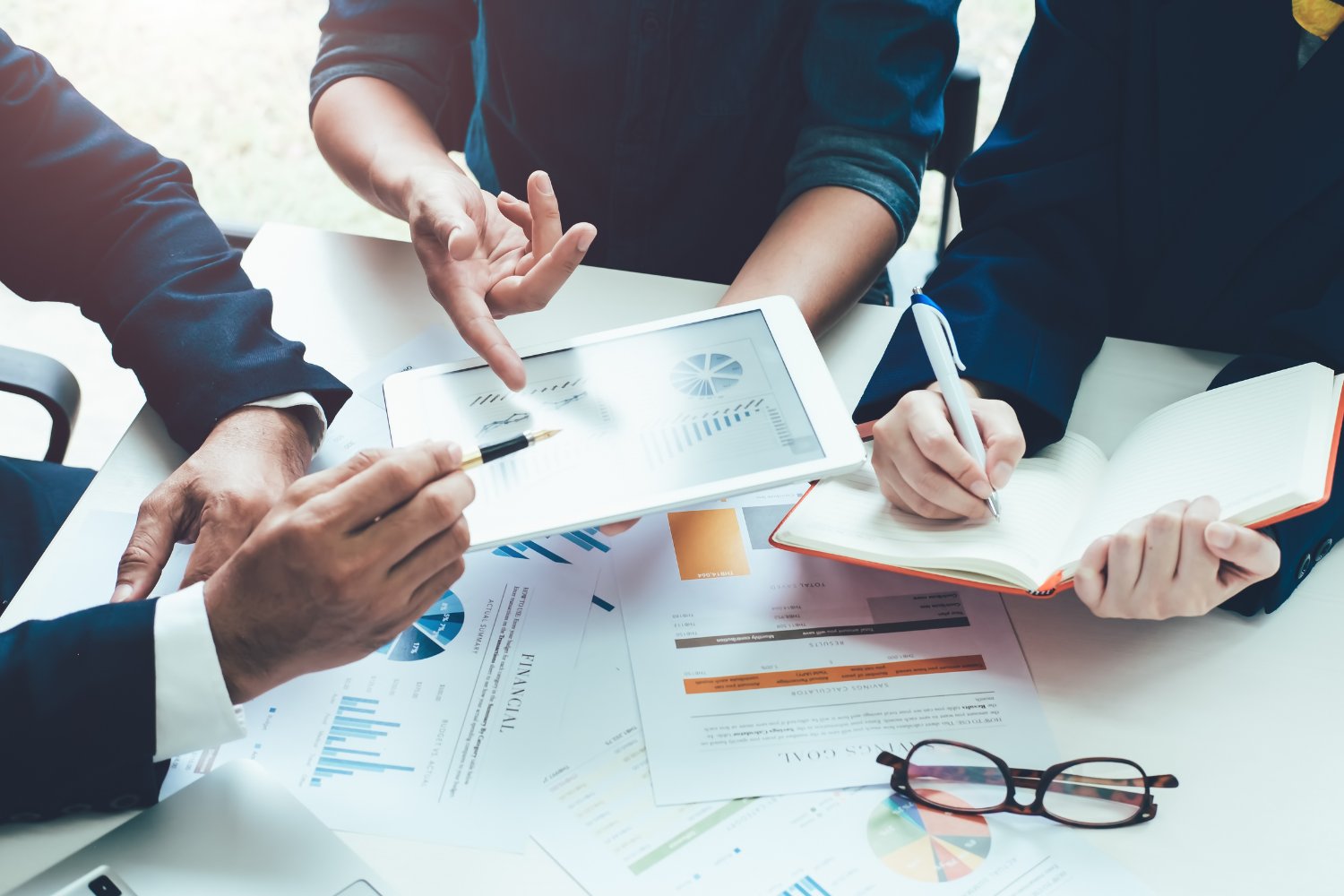 Three people reviewing financial documents and a tablet on a white table.