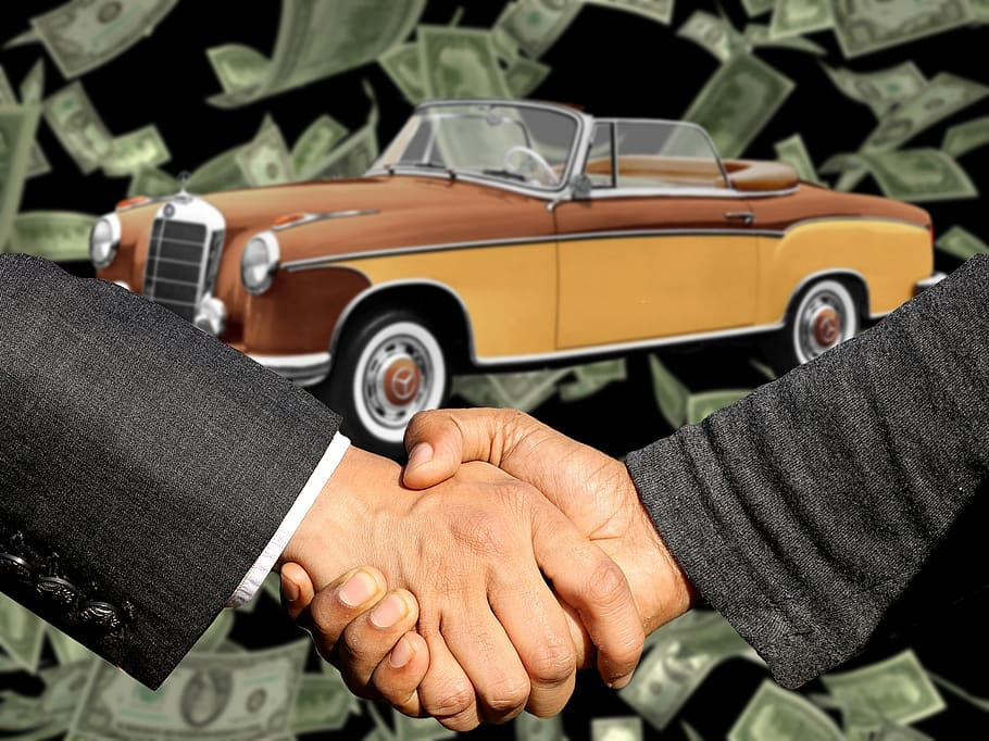 A man holding a stack of cash with a junk car in the background