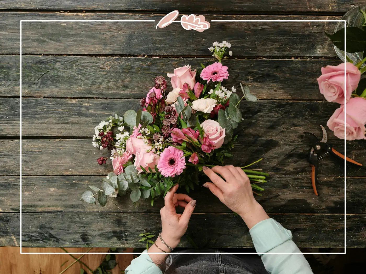 Hands delicately arranging a pink and white floral bouquet on a rustic wooden table, with floral tools scattered around - Fabulous Flowers and Gifts