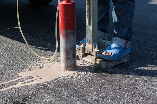 A person drilling a hole in asphalt with a diamond core drill bit