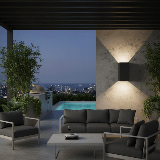 Up-down outdoor wall light fixture illuminating a stylish patio with modern seating, offering a scenic view of the pool and city skyline at night.