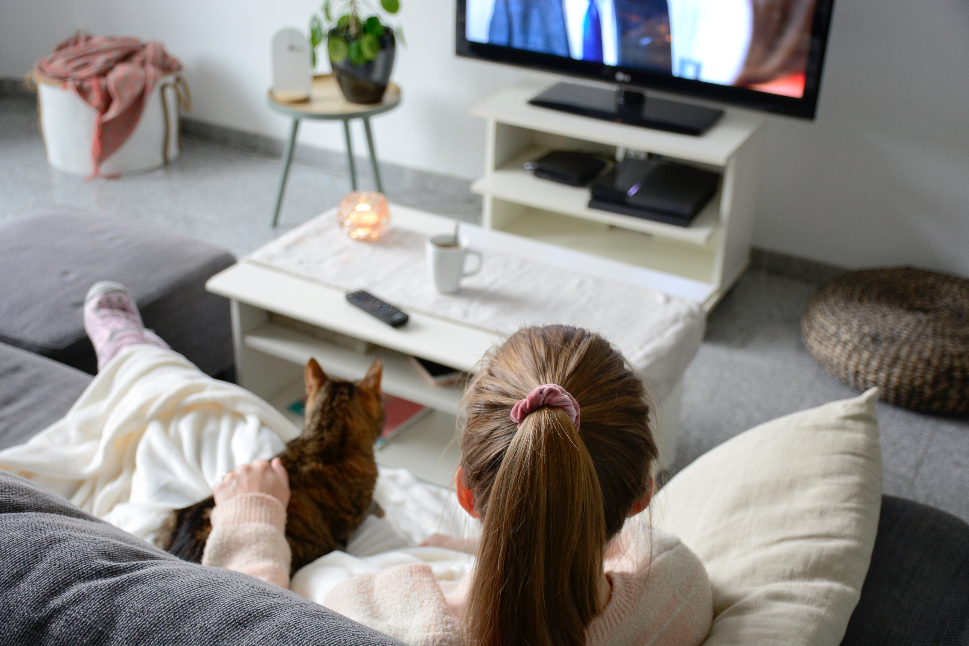 a woman lays down on the couch with her cat while watching television