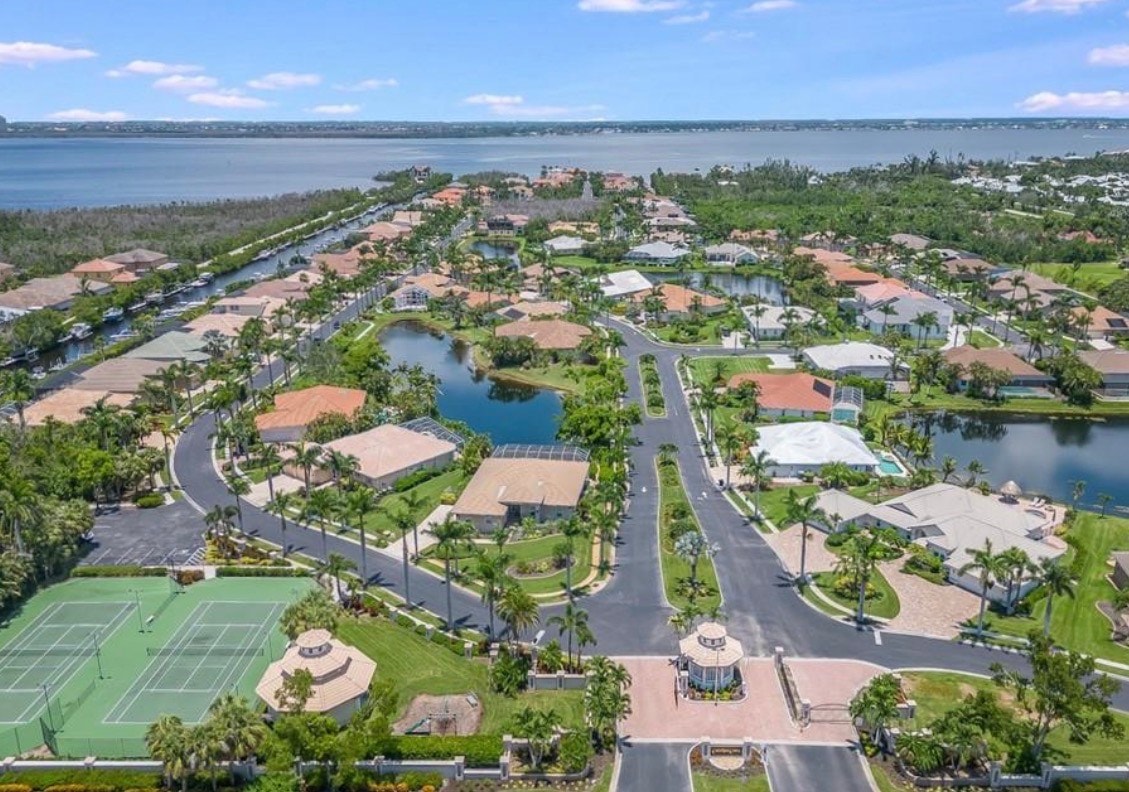 The image depicts tennis courts surrounded by palm trees, set within an upscale gated boating community in Fort Myers, Florida. In the background, waterfront community buildings can be seen, highlighting the scenic views of the Caloosahatchee River and the vibrant lifestyle of Catalpa Cove.