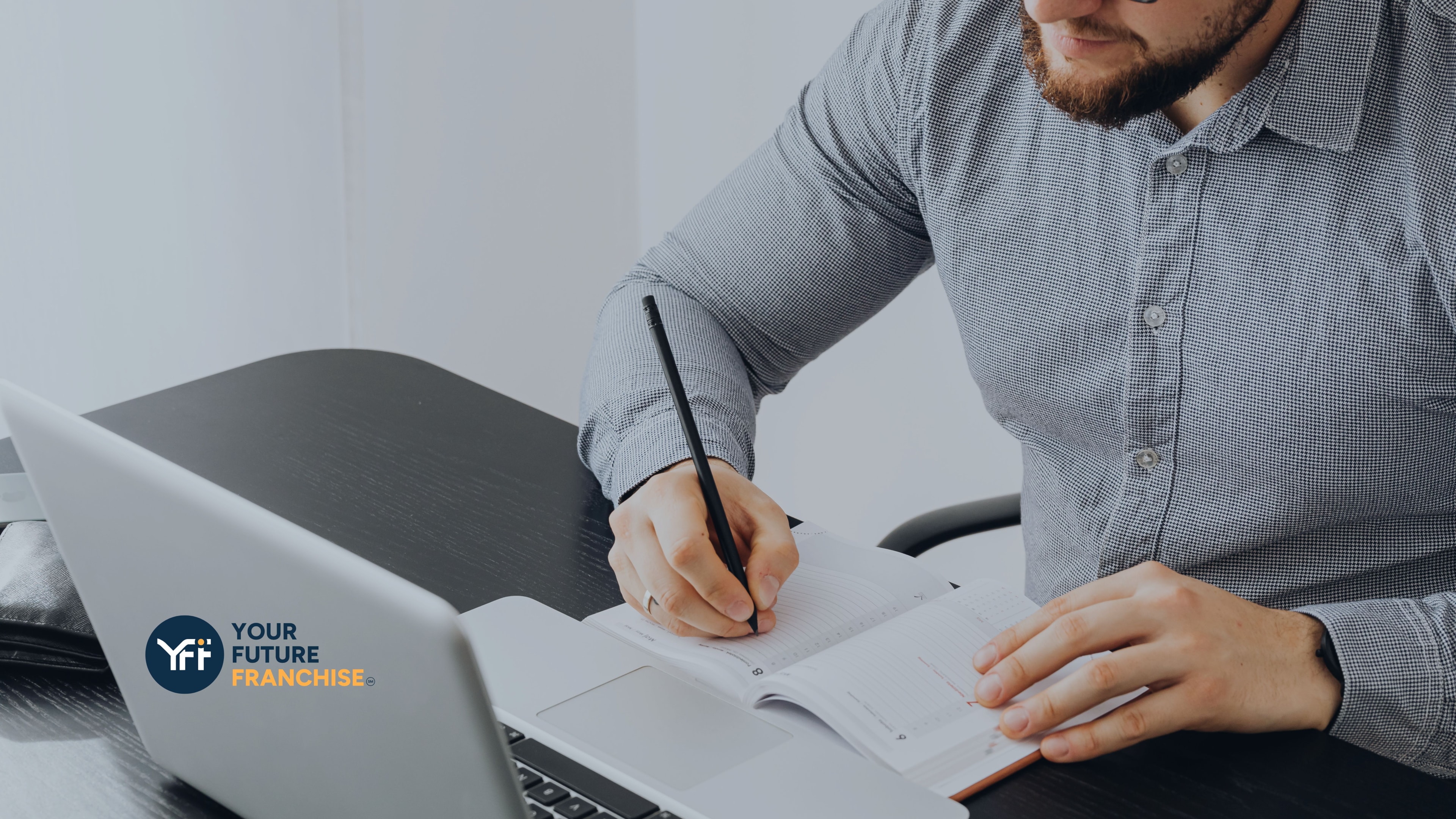 Businessman writing in his diary with his laptop in front of him